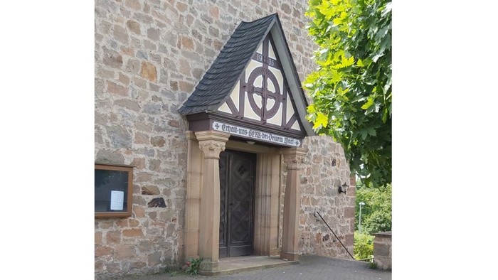 Steingebäude mit Holztür und dreieckigem Dach mit keltischem Design.