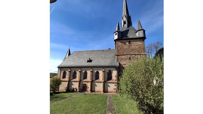 Kirche mit hohem Turm und Ziegelaußenfassade, umgeben von grünem Gras und Sträuchern.