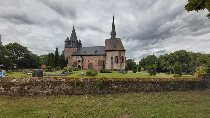 Historische Kirche mit zwei Türmen, umgeben von Grünflächen und einer Steinmauer.