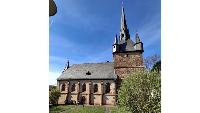 Kirche mit hohem Turm und Ziegelaußenfassade, umgeben von grünem Gras und Sträuchern.