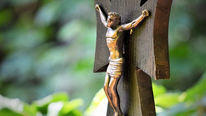 Ein hölzernes Kruzifix hängt an einem Rosenkranz im Garten.