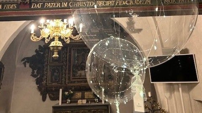 Religiøst alter med krucifiksstatue, globuslamper og latinske inskriptioner over prægtige kirkedekorationer.