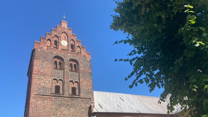 Røde murstenskirke med tårn og spids tak.