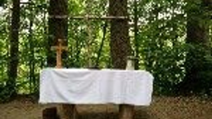 Im Wald steht ein Tisch mit weißer Tischdecke und Stühlen darunter.