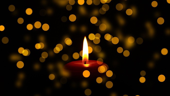 Ein einzelnes brennendes Kerzenlicht vor einem Hintergrund aus goldenen Lichtern.