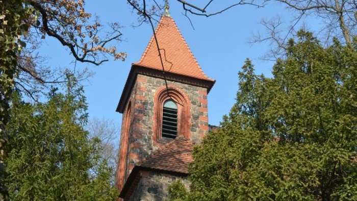 Ein roter Ziegelturm ragt zwischen Bäumen empor