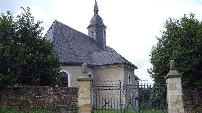 Kleine Kirche mit hohem Turm hinter schwarzem Tor