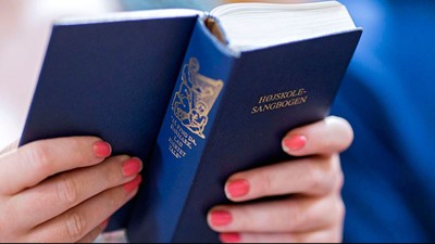 Hands holder blå pas med guldindtryk og teksten "Hauskole-Sangbogen".