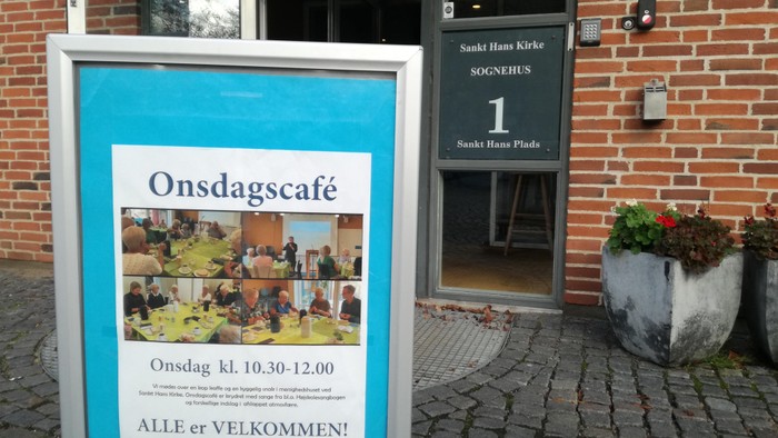 Skilt til en café med åbningstider og en velkomsthilsen.