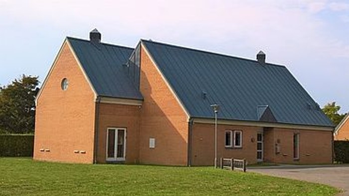 Et rødt teglhus med mørkt tag og en lille træbank foran