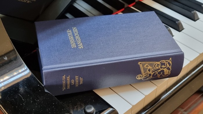 En blå bog med guldindskrift ligger på et piano.