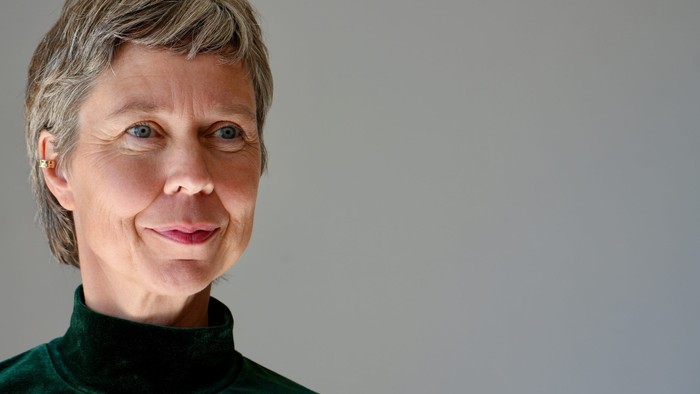 En kvinde med kort hår, iført en grøn rulnekkertrøje, smiler varmt.