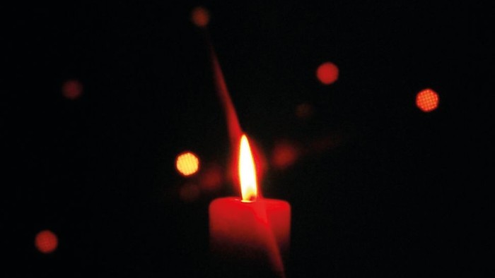 Eine rote Kerze brennt im Dunkeln, umgeben von Lichtpunkten