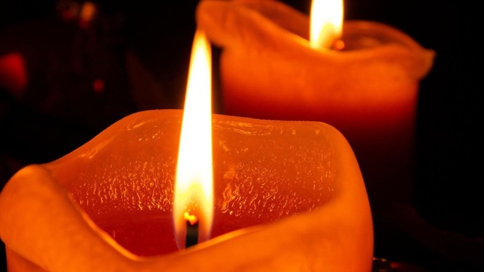 Zwei brennende Kerzen in orangefarbenen Haltern.