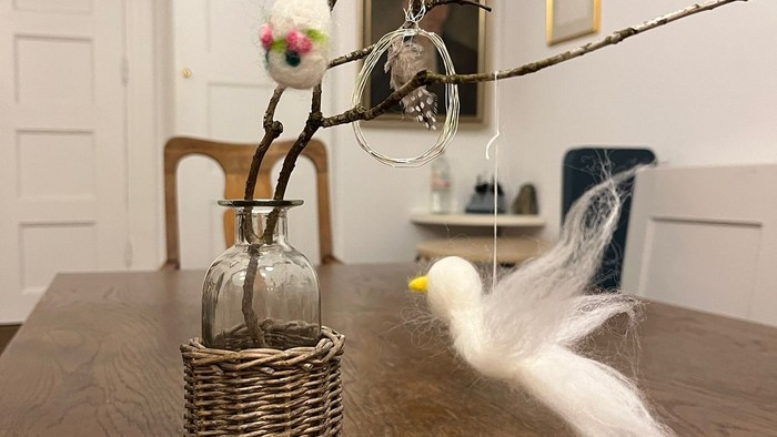 Ein Tisch mit einer Vase und einem Vogel, an der Wand Bilder und ein Stuhl