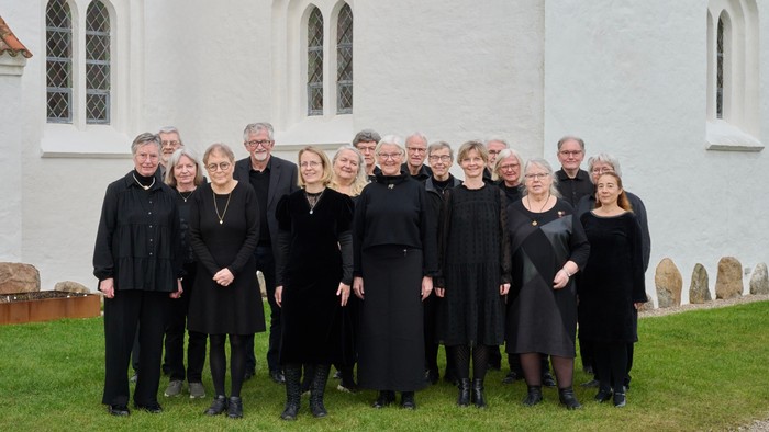 Gruppe af mennesker i formelt sort tøj, der poserer uden for en hvid kirke med buede vinduer.