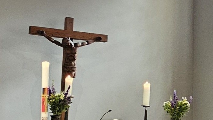 Ein Kirchenaltar mit Kreuz und Kerzen vor einem bunten Fenster