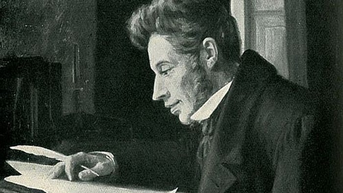 En eftertænksom mand optaget af at læse eller skrive ved et træskrivebord i et svagt oplyst rum.