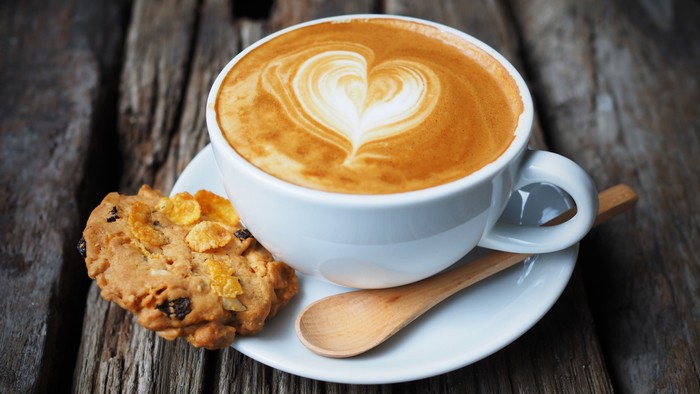 Ein Cappuccino mit Herzverzierung und ein Keks auf einem Holztisch