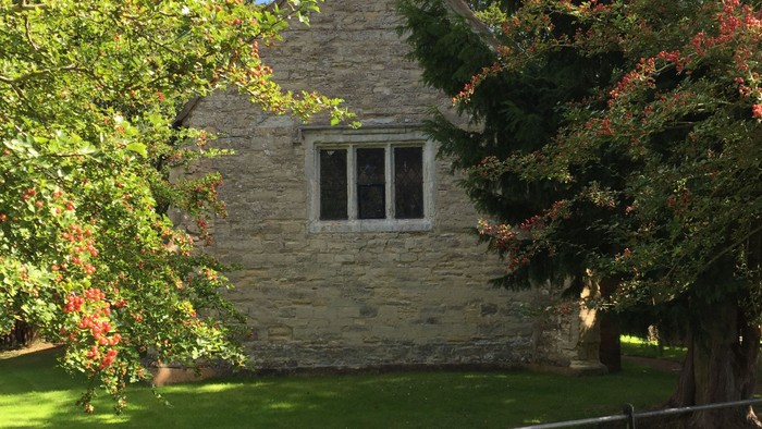 Stone house with steep roof and small window, surrounded by trees and bushes.