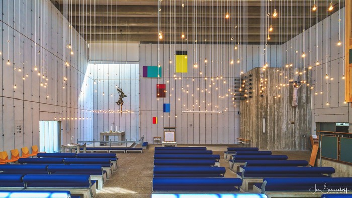 Indre del af moderne kirke med blå bænke og lysstykker.