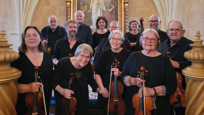 Musikere poserer med instrumenter i en prægtig sal.