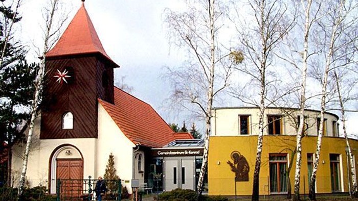 Kleine Kirche mit rotem Dach neben einem gelben Gebäude mit Baum.