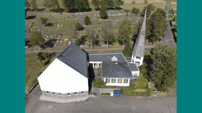 Das Bild zeigt ein weißes Haus mit schwarzem Dach und einem Parkplatz.