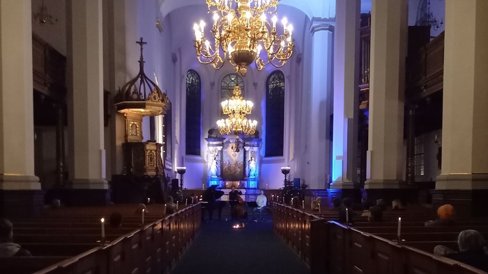 Elegant kirkeinteriør med store lysekroner, dæmpet belysning og lange træbænke, der fører hen til et alter.