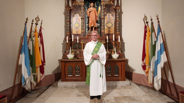 Ein Priester steht vor einem Altar mit Fahnen.