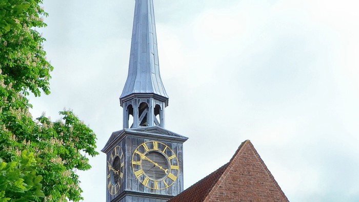 Kirketårn med klokke og spire mod en blå sky