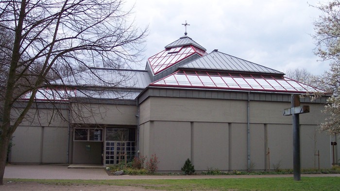 Ein modernes Gebäude mit flachem Dach und Glasfront, umgeben von Bäumen und Gras.