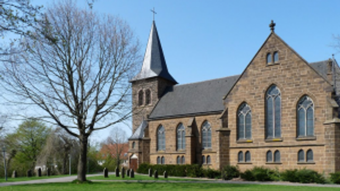 Ein Kirchengebäude mit hohem Turm und spitzen Fenstern steht auf einem grünen Rasen.