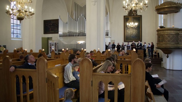 In der Kirche sitzen Menschen in Holzbänken, einige lesen aus Büchern.