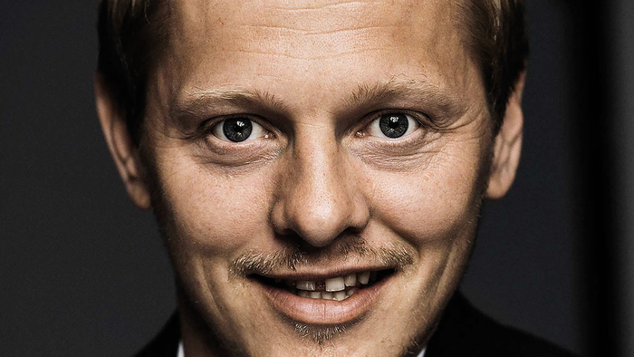Mand i middelalderen med kort hår og overskæg, der smiler let.