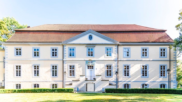 Großes, weißes Gebäude mit blauen Fensterläden und rotem Dach, umgeben von einem grünen Rasen