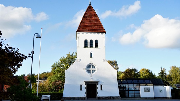 En hvid kirke med rød tagtårn og en rund vindueskærm.
