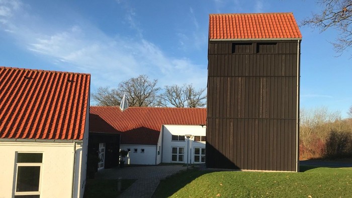 En moderne bygning med rød tag og en høj, træklædt tårn ved siden af en hvid bygning med rød tag og græsplæne foran