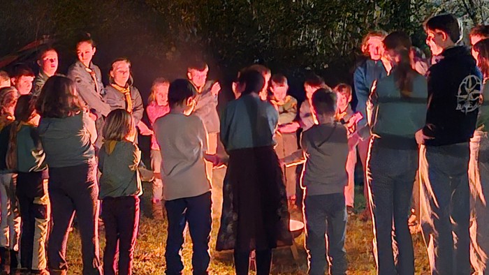 Eine Gruppe von Menschen versammelte sich um ein Lagerfeuer in einer nächtlichen Outdoor-Umgebung und tauschte sich im Gespräch aus.