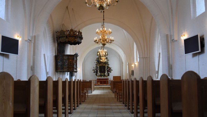 Indre del af kirke med høje vægge og belysning fra kandelier
