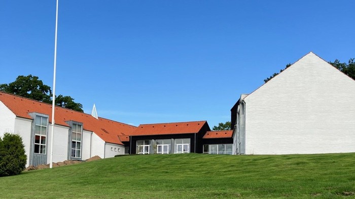 En hvid bygning med røde tag og en flagstang foran