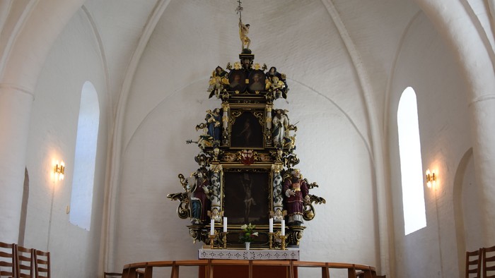 Indre del af kirke med altertavle og bænke.