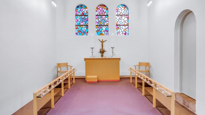 En lille kapel med farverige vinduesglas, alter med krucifix og tre stolene foran
