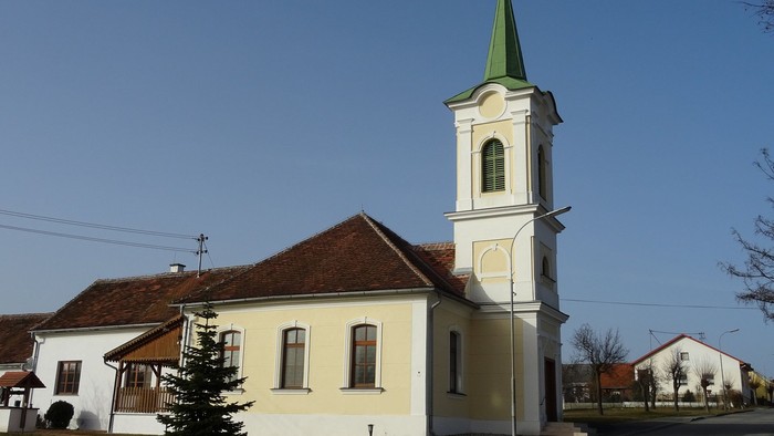 Kleine Kirche mit hohem Turm und grünem Dach in ländlicher Gegend