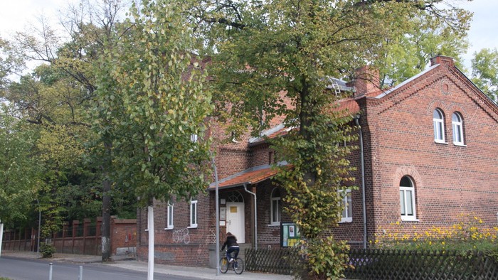 Ein rotes Backsteingebäude mit einem Fahrrad davor und Bäumen daneben