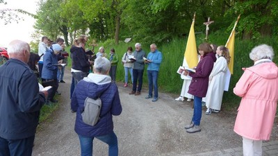 Gruppe von Menschen, die an einer religiösen Prozession im Freien teilnehmen und Banner sowie Bücher halten.