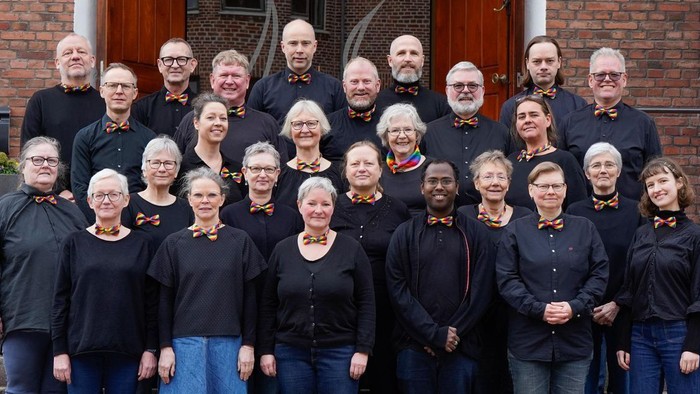 En gruppe af mennesker står sammen i forgrunden af et rødt murværk.