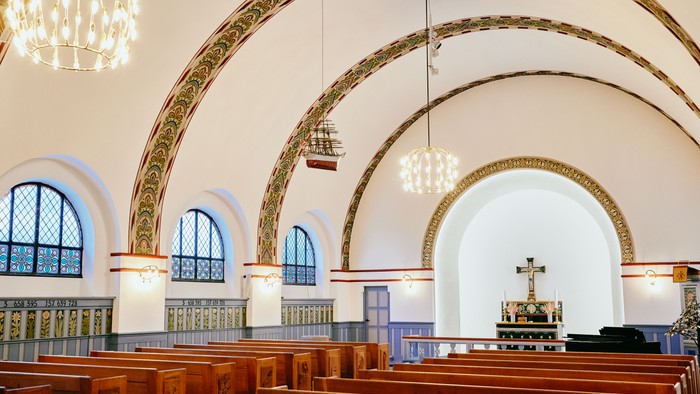 Indre del af kirke med høje buer og træbænke.