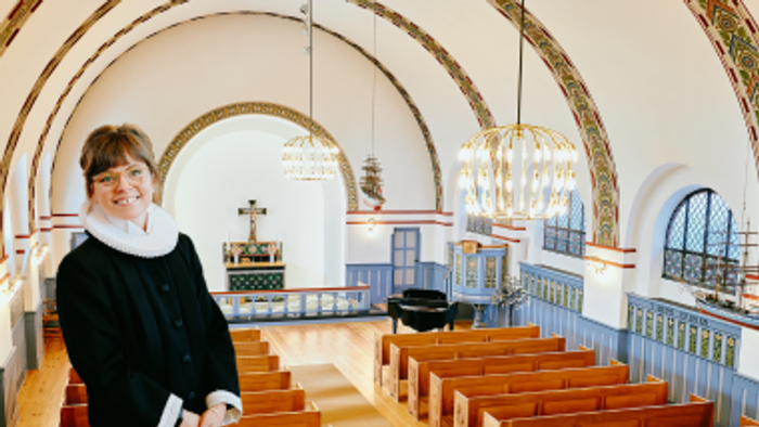 En kvinde står i en kirke med høje buer og træbænke.