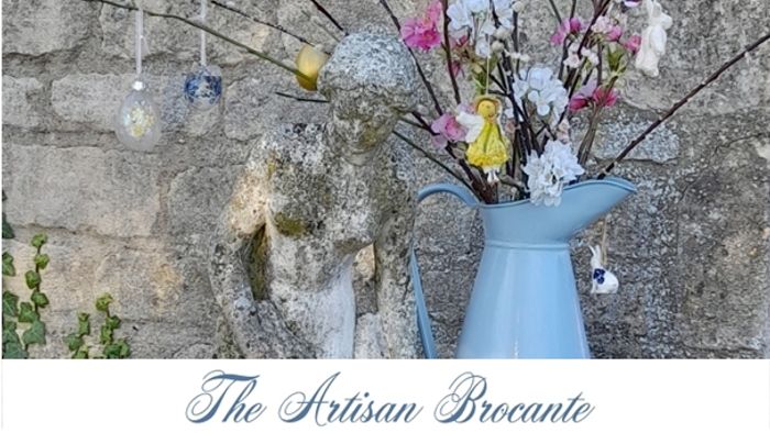 A blue vase with flowers sits against a stone wall, with hanging ornaments nearby